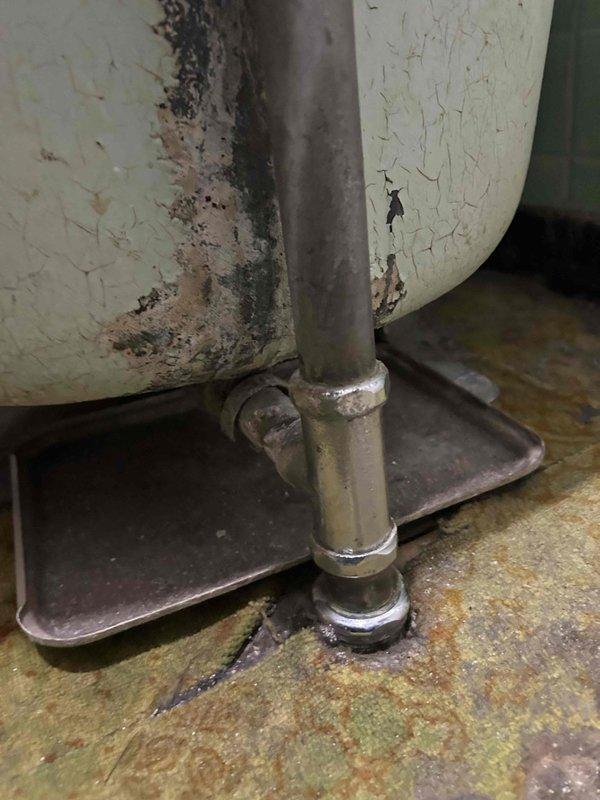 Responded to plumbing leak complaint regarding tub drain. Upon inspection, discovered deteriorated conditions in mechanical/utility area with evidence of moisture intrusion and water damage to surrounding surfaces and equipment. Documented extensive environmental deterioration including staining, mineral deposits, and compromised finishes on nearby water heater and structural surfaces. Assessed drain line connections and identified source of leak requiring repair to prevent further water damage to basement area.