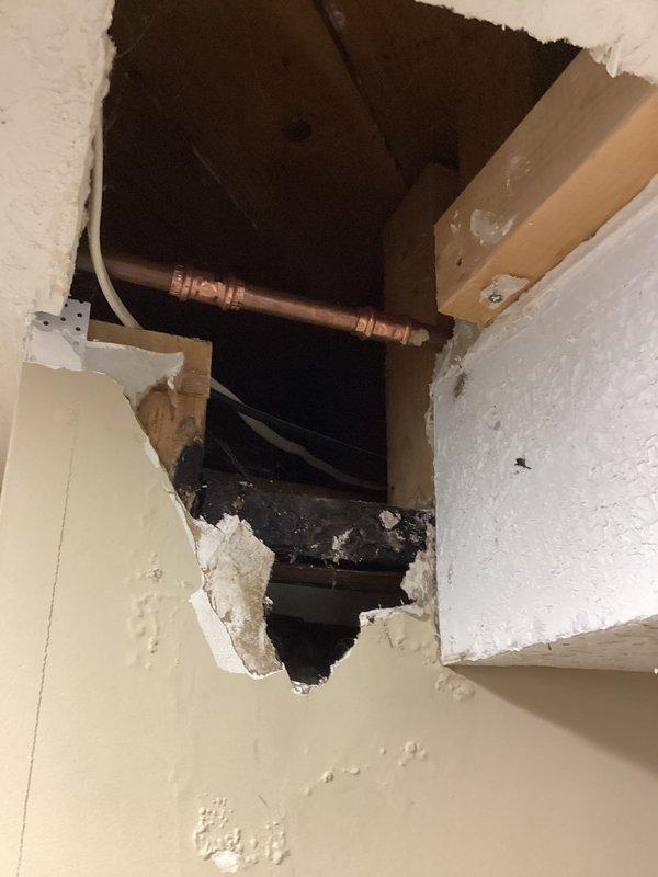 Responded to customer report of water backup in basement. Accessed ceiling and wall cavities to investigate source of water intrusion. Identified copper plumbing line running through affected area with evidence of water damage and staining around opening. Removed drywall sections at ceiling and wall junction to expose plumbing and assess extent of damage. Located leak source and documented conditions with photos showing exposed pipe, wiring, and framing members in compromised area.