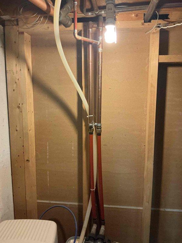 Responded to a water softener leak that had been active for approximately 90 days in a 1969-built home. Upon inspection of the basement utility area, identified the leak source at the water softener plumbing connections. The system consisted of dual water treatment units with copper supply lines and PEX distribution piping mounted on a plywood backing panel. Assessed the vertical piping assembly including shut-off valves, fittings, and connections to determine the exact point of water intrusion. Documented the condition of both the water softener unit and associated brine tank with pump assembly, noting moisture staining on the concrete floor at the base of the units. Photographed the complete plumbing configuration including copper pipes, flexible tubing connections, and control valves for service records. Completed necessary repairs to eliminate the leak and restore proper system operation.