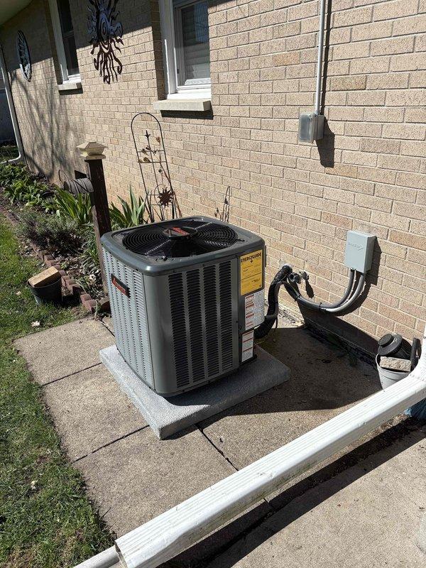 Successfully completed full air conditioning system installation including outdoor condenser unit and indoor air handler. Condenser was positioned on concrete pad adjacent to building exterior with proper refrigerant line routing, electrical disconnect installation, and secure mounting of all components. Indoor air handler was installed in basement mechanical room alongside existing HVAC equipment with black flexible ductwork connections, PVC condensate drain line, and all required electrical connections completed per manufacturer specifications.