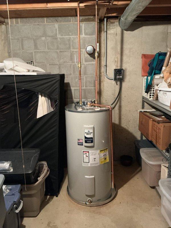 Completed conversion from gas to electric water heater installation in basement utility area. Installed customer-supplied electric water heater with proper copper piping connections, pressure relief valve assembly, and required electrical disconnect box mounted to wall per code requirements. All plumbing connections secured and tested, unit operational and ready for service.