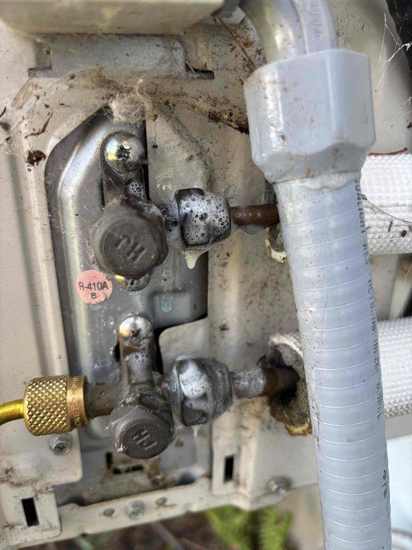 Responded to no cooling complaint on 6-year-old Daikin system with recent circuit board warranty replacement. Performed refrigerant leak inspection at service valves and identified potential leak points at valve connections showing corrosion and age-related degradation. Documented equipment condition with photos showing R-410A refrigerant system components, service ports, and areas of concern for further leak detection and repair recommendations.