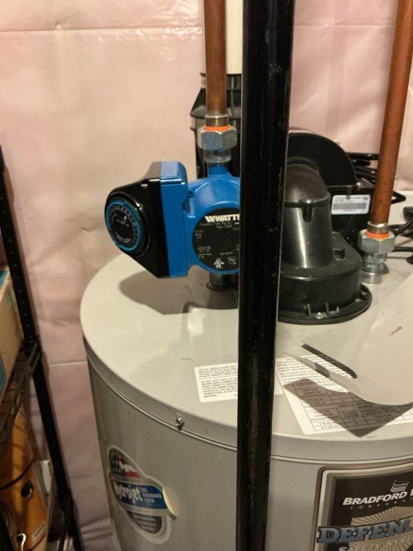 Evaluated existing 11-year-old residential water heater that has completely failed and is no longer operational. Documented current installation including white cylindrical tank water heater with blue Watts circulation pump, copper piping configuration, and integrated black water treatment system. Assessed plumbing connections, mechanical room layout with exposed framing and insulation, and utility infrastructure including gas lines and drainage systems. Provided estimate for complete water heater replacement to restore hot water service to the residence.