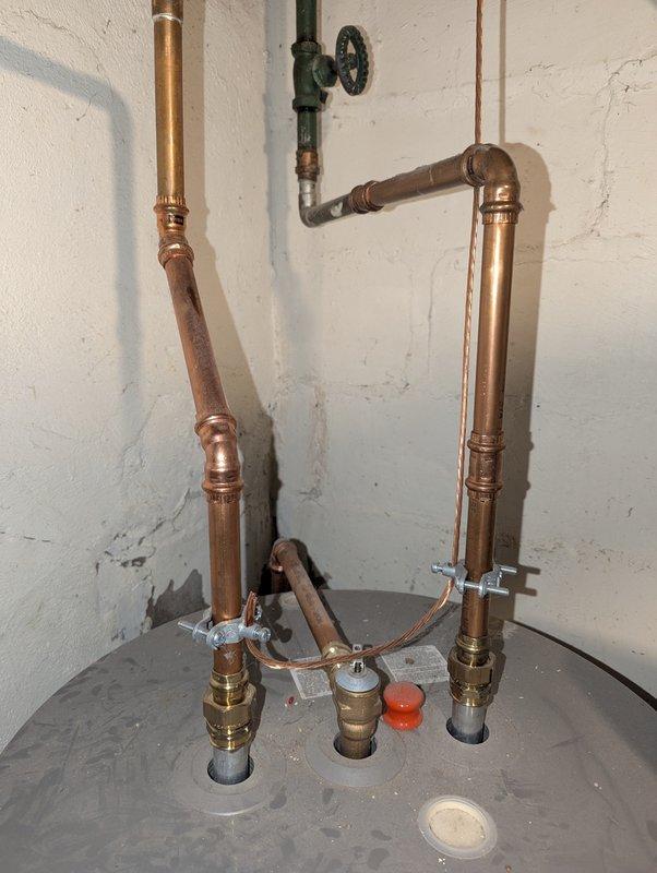 Completed estimate for replacement of 8-year-old Rheem water heater. Assessed existing plumbing configuration including copper piping with multiple vertical sections, brass fittings, and wall-mounted shut-off valve. Documented current installation featuring Pentair water treatment device mounted atop blue filtration tank with interconnected plumbing system showing moderate oxidation and wear patterns.