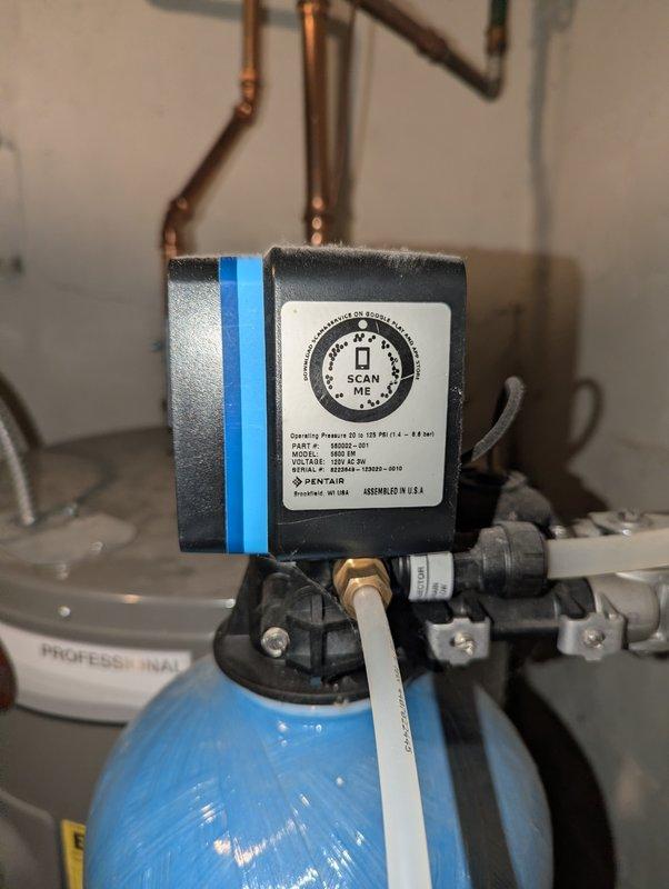 Completed estimate for replacement of 8-year-old Rheem water heater. Assessed existing plumbing configuration including copper piping with multiple vertical sections, brass fittings, and wall-mounted shut-off valve. Documented current installation featuring Pentair water treatment device mounted atop blue filtration tank with interconnected plumbing system showing moderate oxidation and wear patterns.
