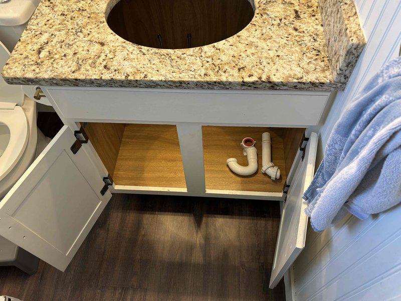 Completed installation of customer-supplied undermount lavatory sink and faucet in bathroom vanity. Removed existing fixture, prepared granite countertop opening, secured undermount sink basin, connected P-trap drainage assembly with white PVC piping, and installed new faucet with complete water supply connections.