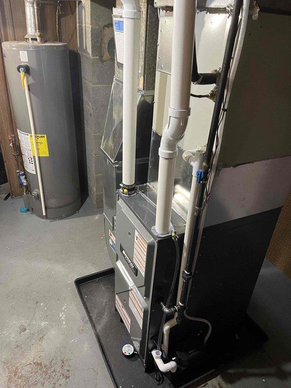 Completed full furnace installation in basement utility room. Installed new gray furnace unit on protective drip pan with proper PVC venting and metal flue piping routed vertically through ceiling. Connected unit to existing ductwork system including silver air handler with digital control panel. Secured all manufacturer labels and specifications on equipment panels. Verified proper clearances from water heater and foundation walls. Tested system operation and confirmed all connections meet code requirements.