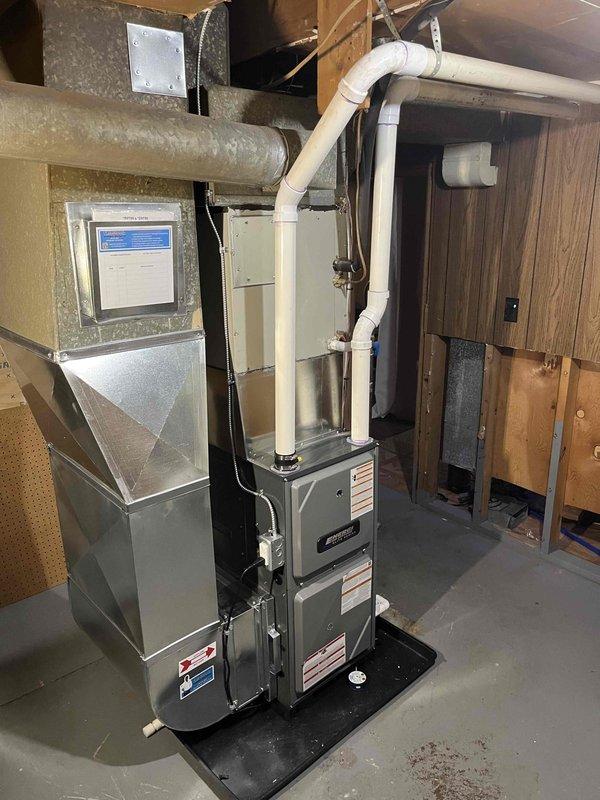 Completed full furnace installation in basement utility room. Installed new gray furnace unit on protective drip pan with proper PVC venting and metal flue piping routed vertically through ceiling. Connected unit to existing ductwork system including silver air handler with digital control panel. Secured all manufacturer labels and specifications on equipment panels. Verified proper clearances from water heater and foundation walls. Tested system operation and confirmed all connections meet code requirements.