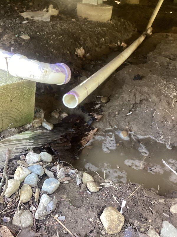 Responded to emergency plumbing leak in crawl space where broken elbow joint between two pipes was actively spraying water near the foundation. Upon arrival, assessed the damaged connection and shut off water supply to stop active spray. Removed failed elbow fitting and cleaned pipe ends of debris and old primer. Installed new PVC elbow joint with proper purple primer and solvent cement application, ensuring secure watertight connections on both pipe ends. Verified repair integrity by restoring water pressure and inspecting for leaks. Placed river rocks around affected area to improve drainage and prevent soil erosion from previous water damage. Documented standing water and muddy conditions in crawl space resulting from the leak. Repair completed successfully with no further water discharge observed.