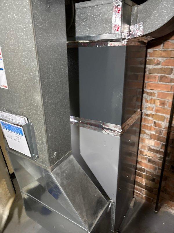 Completed full air conditioning system replacement including outdoor condensing unit and indoor air handler components. Installed new outdoor unit on concrete pad with proper refrigerant line routing along exterior wall, secured with mounting brackets. Replaced indoor ductwork assembly in basement utility area, including vertical rectangular duct section and transition pieces with proper sealing at all metal joints and connections.
