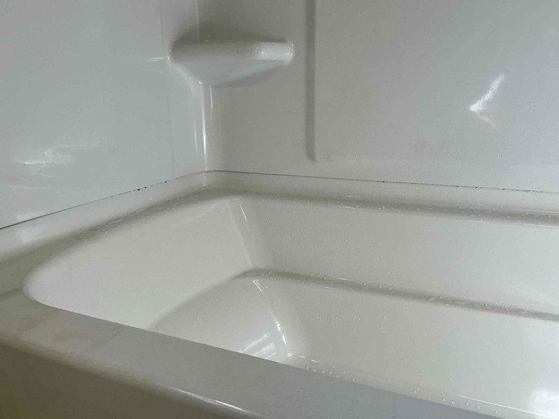 Completed full shower surround replacement in bathroom. Removed existing deteriorated wall materials and fixtures, exposing framing and studs. Installed new white molded fiberglass bathtub and shower surround unit with integrated corner shelving.