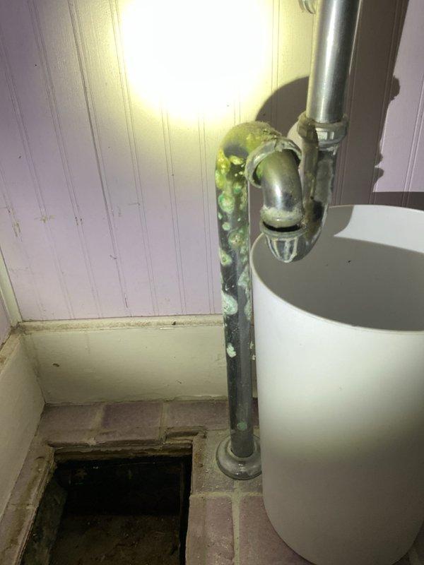 Responded to a second-floor bathroom sink leak complaint. Upon inspection, discovered heavily corroded vertical drain pipe with significant green oxidation and deterioration beneath the sink. The existing P-trap and drainage system showed signs of long-term water damage and corrosion. Assessed the full extent of pipe degradation from the sink connection down through the floor opening. Documented the temporary drainage setup with collection bucket due to compromised pipe integrity. Recommended complete replacement of corroded drainage pipes and P-trap assembly to restore proper function and prevent further water damage to surrounding floor structure and subflooring.
