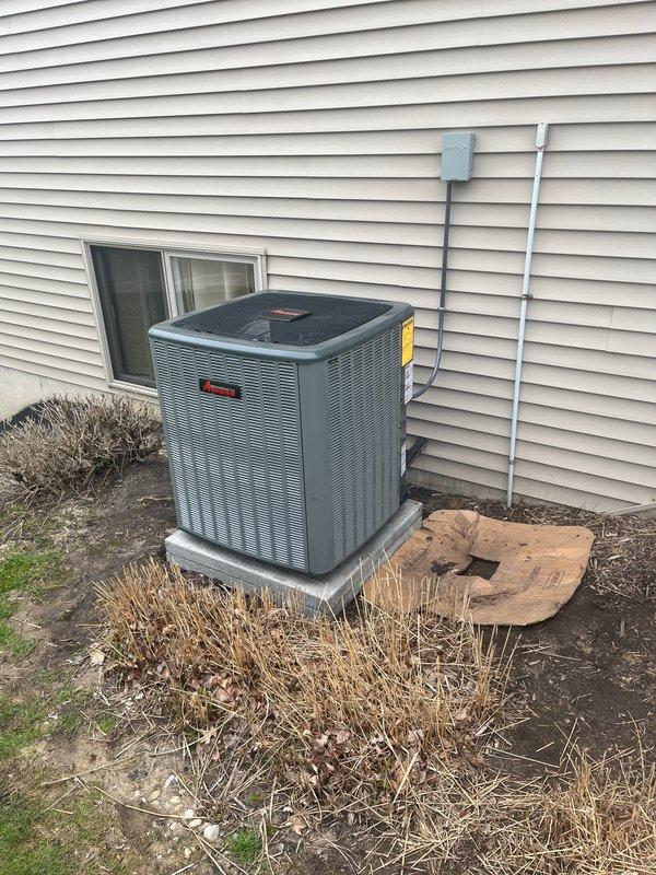 Completed full HVAC system installation including new Amana air conditioning condenser unit and furnace. Mounted outdoor AC unit on concrete pad against exterior wall with proper clearances, installed refrigerant line sets with gray and white conduit runs up vinyl siding to electrical disconnect box. Interior installation included new gas furnace in basement mechanical room with complete ductwork connections to existing distribution system. Installed white PVC venting from furnace through ceiling joists, connected all supply and return ductwork using rectangular and cylindrical metal ducts. Verified proper electrical connections, tested system operation for heating and cooling functions, confirmed all safety controls and limit switches functioning correctly. Placed protective mat under furnace, ensured all manufacturer labels and warning stickers properly affixed to equipment. System commissioned and left in full operational status.