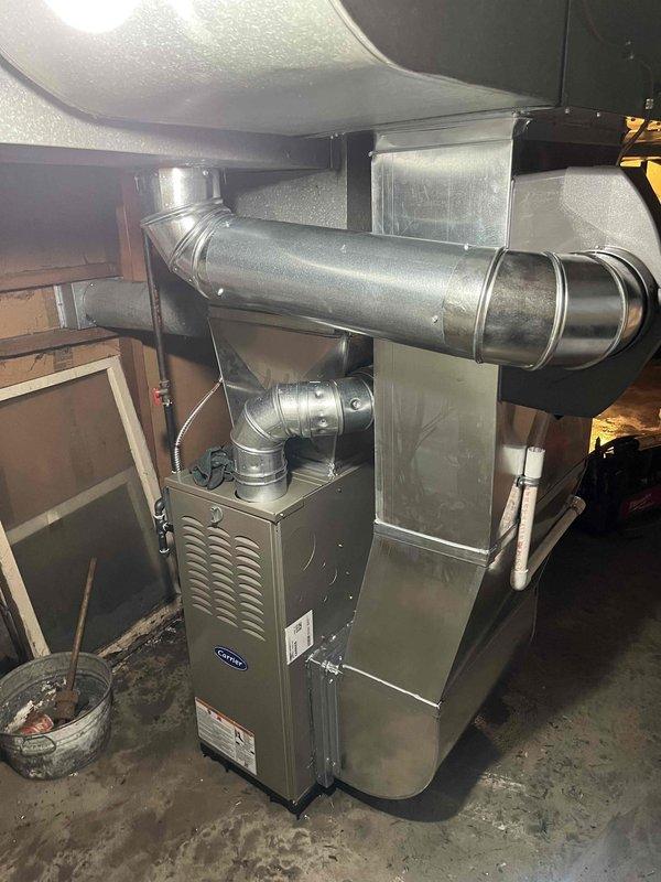 Completed full furnace replacement with installation of new Carrier gas furnace unit in residential basement location. Connected metallic supply ductwork with horizontal trunk line and elbow joint to existing distribution system. Installed unit against brick wall with proper clearances, secured all ductwork connections, verified proper venting, tested system operation, and confirmed heating functionality upon completion.