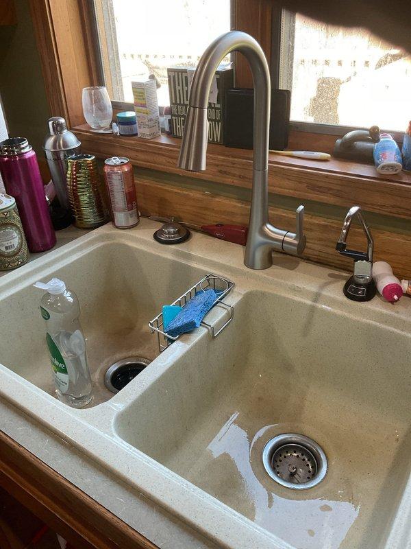 Completed kitchen faucet installation on double basin composite sink with butcher-block countertop. Installed brushed stainless steel faucet with high-arc spout and matching side spray assembly, ensuring proper connections to existing supply lines and adequate clearance for sink operation. Verified all plumbing connections beneath sink were secure, tested water flow and spray functions, and confirmed no leaks at supply lines or drain connections.