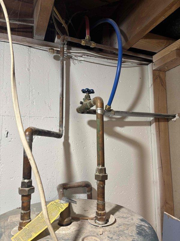 Responded to service call for leaking 20-year-old electric water heater in basement. Inspected 50-gallon unit and documented existing plumbing connections, including copper supply lines, brass shutoff valve with blue handle, flexible connectors, and associated fittings. Photographed installation showing aging infrastructure and provided estimate for water heater replacement due to unit reaching end of serviceable life.
