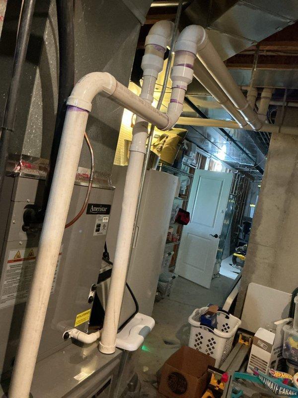 Rerouted furnace exhaust piping system in basement mechanical room to correct improper venting configuration. Installed new white PVC exhaust pipes with proper support brackets and purple mounting straps, ensuring code-compliant vertical and horizontal runs with appropriate pitch for condensate drainage. System tested and verified operational upon completion.