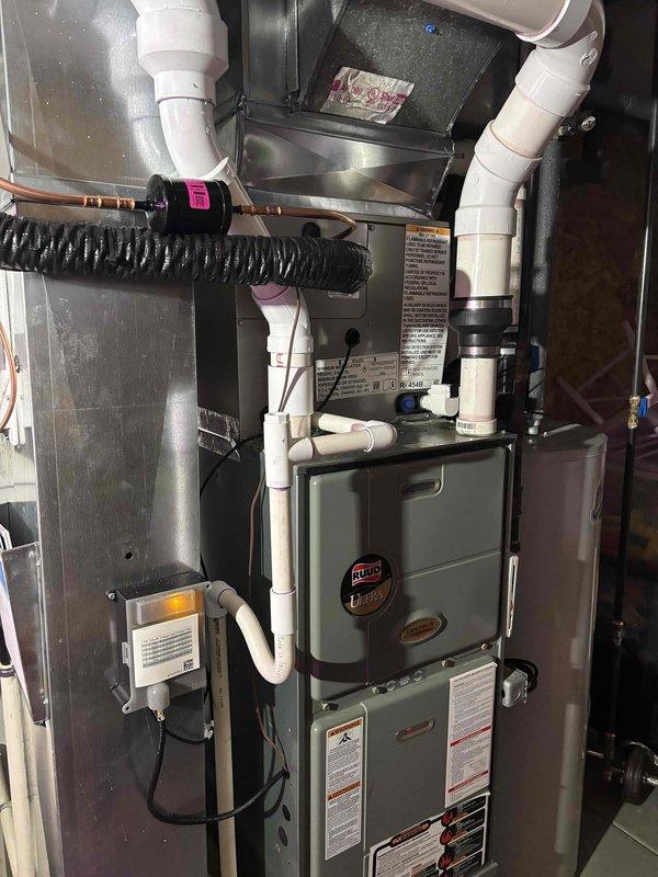 Completed full HVAC system replacement including installation of new Ruud furnace unit in basement utility area and outdoor condensing unit on concrete pad. Installed all refrigerant line sets with proper insulation, white PVC condensate drainage piping, and black corrugated drain lines with appropriate fittings and connections. Mounted outdoor condenser unit with protective line set guard, connected all electrical components, and verified proper system operation upon startup.