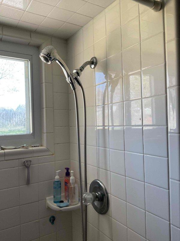 Replaced single-handle shower fixture with chrome handheld showerhead assembly and control valve. All fixtures installed and tested for proper operation with no leaks detected.