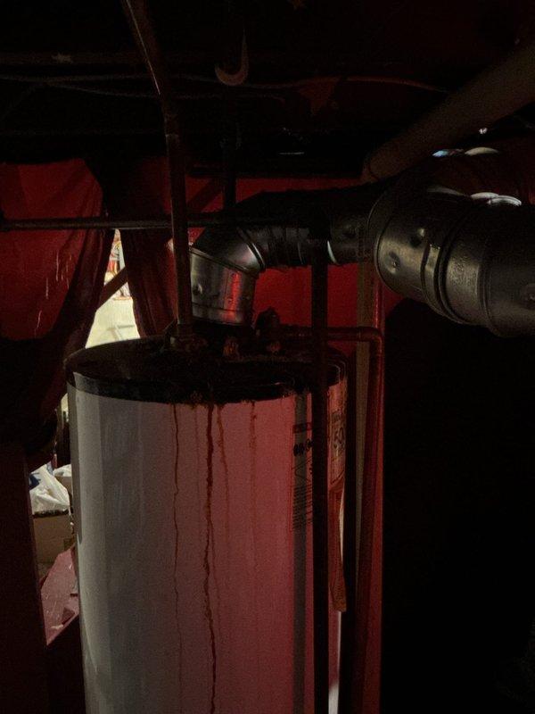 Provided estimate for replacement of thirty-year-old water heater showing significant rust staining and deterioration. Unit exhibits visible corrosion on exterior surfaces and rust accumulation at base, indicating end of serviceable life expectancy. Documented existing installation conditions including plumbing connections and utility space configuration for replacement planning.