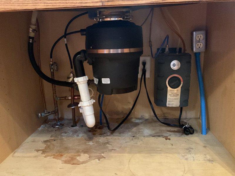 Responded to plumbing leak concern involving reverse osmosis system and potential beverage dispenser connection. Upon inspection, located leak source in under-sink cabinet area affecting garbage disposal plumbing connections and surrounding fixtures. Identified water damage and staining on cabinet floor indicating previous moisture exposure. Examined all connections including PVC drain lines, rubber hoses, water supply lines, and disposal unit fittings. Traced plumbing lines through ceiling cavity to verify system integrity and rule out secondary leak points. Documented existing conditions with photographic evidence showing cabinet interior, disposal assembly, electrical connections, and overhead plumbing runs. Addressed leak at source connection point and verified all related plumbing components for proper operation.