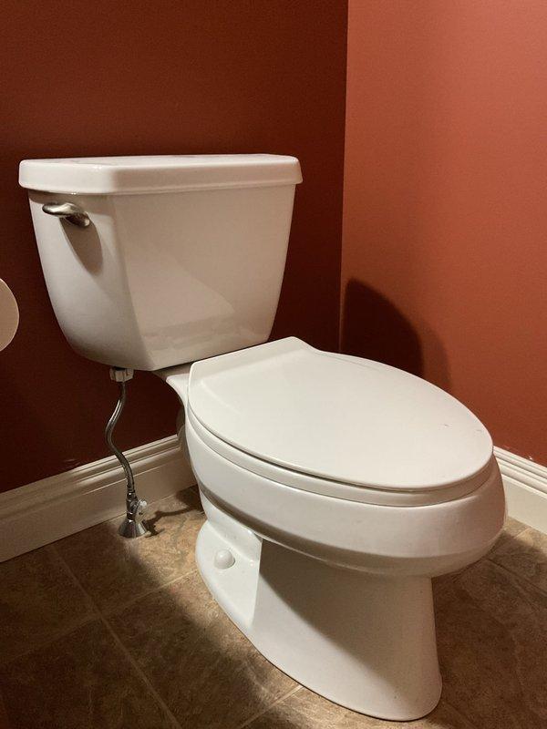 Responded to report of leaky toilet in 22-year-old residential property. Upon arrival, inspected standard two-piece white porcelain toilet with visible water supply line and shut-off valve. Identified source of leak and performed necessary repairs to resolve water seepage issue. Tested toilet operation following repair to confirm proper function and verify leak was fully eliminated. Documented conditions with photographs showing toilet installation, surrounding bathroom environment, and completed repair work.