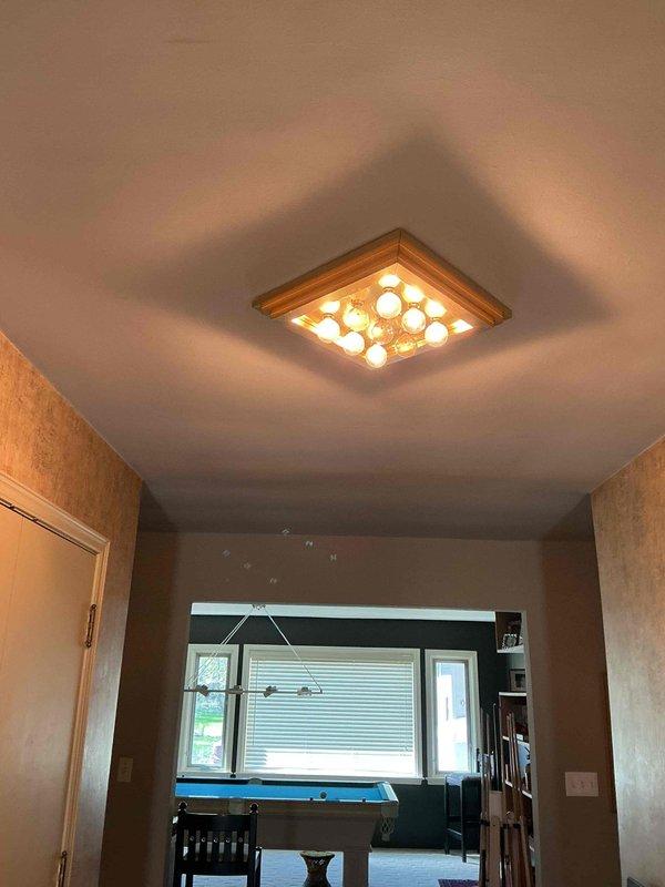 Responded to service call for two non-functioning overhead light fixtures in older residential property. Upon arrival, verified both fixtures in question were inoperative while remaining electrical circuits functioned normally. Inspected flush-mount ceiling fixture with multi-bulb grid configuration in recreation room area and associated three-gang switch control. Troubleshot circuit, identified failed lamp components, and replaced defective bulbs in both overhead fixtures. Verified proper switch operation and restored full functionality to both lighting circuits. All fixtures tested and confirmed operational upon completion.