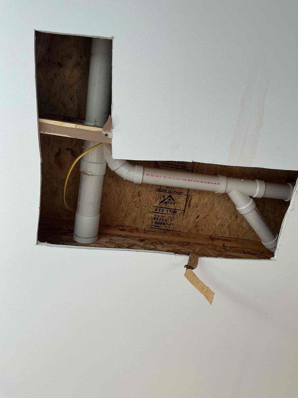 Completed drain repair requiring access through ceiling. Cut access opening in drywall to expose plumbing infrastructure above, where white PVC drain lines and vent pipes were located and repaired. Work included addressing drainage system components, with all plumbing connections restored to proper working condition. Access opening left available for inspection, with repair completed as quoted.
