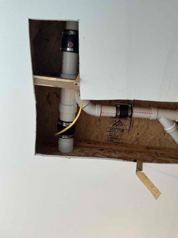 Completed drain repair requiring access through ceiling. Cut access opening in drywall to expose plumbing infrastructure above, where white PVC drain lines and vent pipes were located and repaired. Work included addressing drainage system components, with all plumbing connections restored to proper working condition. Access opening left available for inspection, with repair completed as quoted.