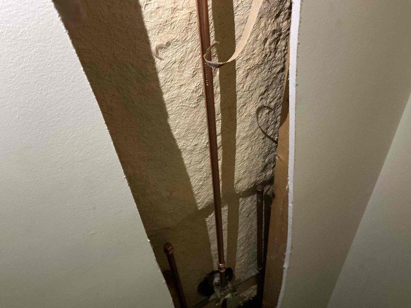 Responded to water leak originating from upstairs shower area. Accessed ceiling and wall cavities to locate source of leak, exposing copper supply lines and plumbing connections. Identified leak point at pipe fitting, documented conditions with photos showing spray foam insulation and copper piping configuration within wall structure for further repair assessment.