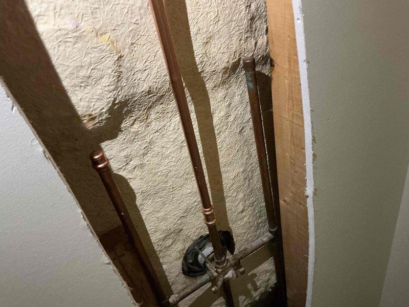 Responded to water leak originating from upstairs shower area. Accessed ceiling and wall cavities to locate source of leak, exposing copper supply lines and plumbing connections. Identified leak point at pipe fitting, documented conditions with photos showing spray foam insulation and copper piping configuration within wall structure for further repair assessment.
