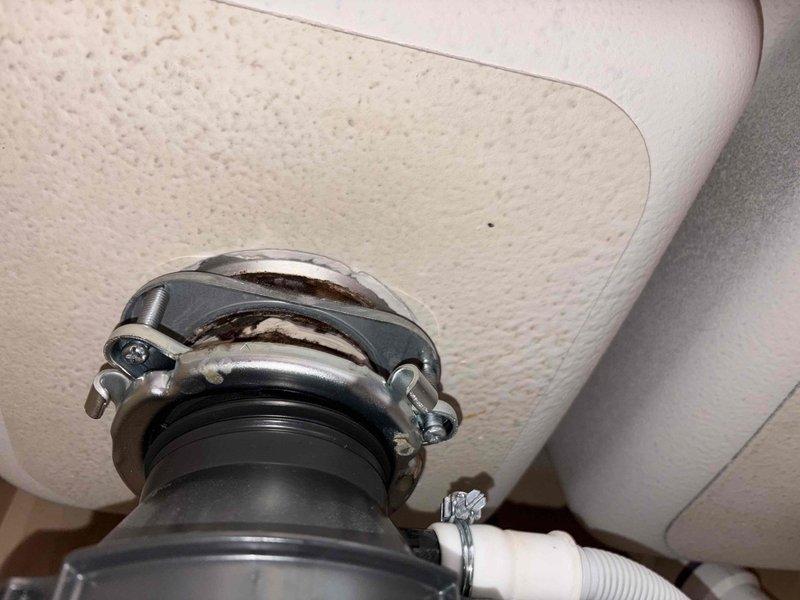 Responded to plumbing leak under kitchen sink in century-old home where customer reported active leak for approximately one week. Upon inspection, identified deteriorated flexible rubber connector with visible wear and staining around metal band clamps at connection points. Assessed drain assembly components including chrome tailpiece with mounting hardware showing signs of water exposure and discoloration on surrounding cabinet materials. Documented existing conditions with photographs showing compromised connections and water damage indicators. Provided customer with repair recommendations to address the leak source and prevent further water intrusion beneath sink cabinet.