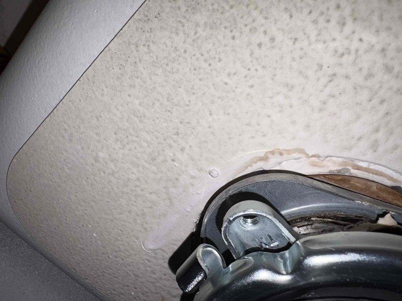Responded to plumbing leak under kitchen sink in century-old home where customer reported active leak for approximately one week. Upon inspection, identified deteriorated flexible rubber connector with visible wear and staining around metal band clamps at connection points. Assessed drain assembly components including chrome tailpiece with mounting hardware showing signs of water exposure and discoloration on surrounding cabinet materials. Documented existing conditions with photographs showing compromised connections and water damage indicators. Provided customer with repair recommendations to address the leak source and prevent further water intrusion beneath sink cabinet.