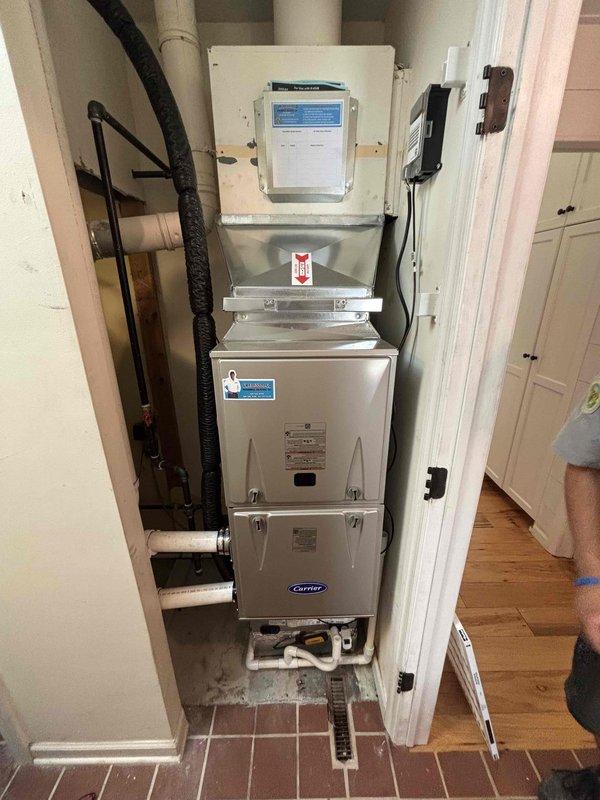 Completed full HVAC system installation including new Carrier furnace and air conditioning unit in residential utility closet. Installed stacked air handler configuration with integrated control panel and thermostat interface, ensuring proper mounting, electrical connections, and ductwork integration with black flexible ducting and metal brackets. Configured all necessary PVC drainage lines, verified proper clearances in mechanical room space, and confirmed system operation with all manufacturer specifications met for heating and cooling functionality.