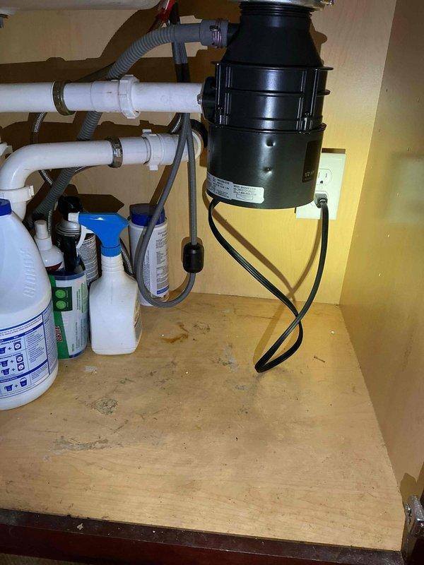 Responded to kitchen sink garbage disposal issue in 25-year-old home. Upon inspection, confirmed disposal unit required replacement due to operational failure. Removed existing disposal unit and installed new black garbage disposal beneath kitchen sink, ensuring proper mounting to sink basin. Connected unit to existing white PVC drain plumbing system with appropriate fittings and secured all connections with metal clamps. Verified electrical connection to cabinet outlet and tested disposal for proper operation. Confirmed all plumbing connections leak-free and disposal functioning correctly. Unit covered under one-year warranty for parts and labor from installation date of 7/25.