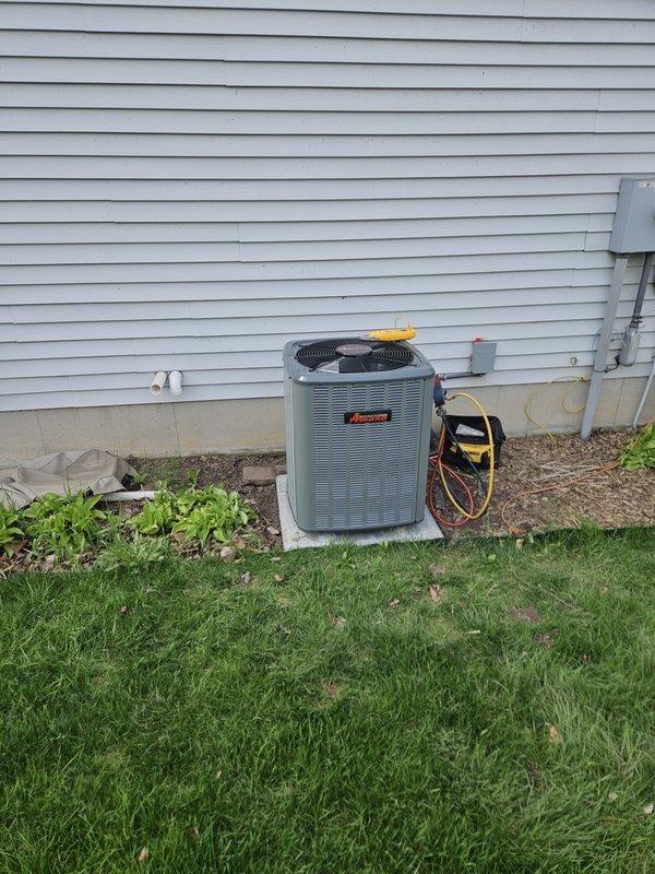 Complete HVAC system replacement performed, including installation of new furnace and air conditioning unit. Furnace installed in basement utility area with air handler positioned adjacent, connected via white PVC condensate drainage system and integrated black flexible ductwork. Outdoor condenser unit installed on stone base against exterior wall with proper refrigerant line connections, electrical disconnect box, and service access. System charged, tested, and verified operational upon completion.