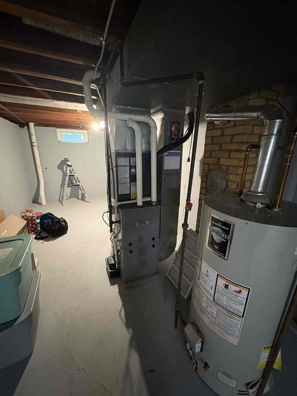 Completed full HVAC system replacement including indoor air handler unit installed in basement utility room and outdoor condensing unit positioned on concrete pad against exterior foundation wall. Both units properly connected with refrigerant lines, electrical service, and condensate drainage per manufacturer specifications. System tested and verified operational.