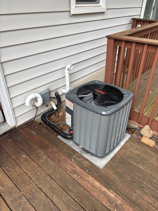Completed full installation of residential HVAC system including furnace, air conditioning unit, and water heater. Exterior AC condenser unit was mounted on white pad on wooden deck with proper refrigerant line routing and PVC condensate drainage connected to home's exterior wall. System was factory-charged with refrigerant per manufacturer specifications, service valves were installed with protective caps, and all connections were properly secured and tested for operation.