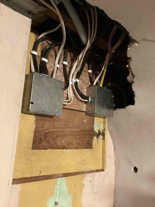 Completed electrical inspection correction involving exposed wall cavity and circuit breaker panel. Accessed interior wall opening to inspect and document two gray electrical junction boxes mounted on horizontal blocking, with multiple electrical wires (white, gray, brown, and yellow) properly routed through the cavity and secured with cable clamps. Photographed circuit breaker panel showing properly labeled circuits for all household systems including surge protection, dryer, stove, bedrooms, deck, GFI outlets, and counter receptacles. Verified all electrical connections within junction boxes meet code requirements and documented existing conditions for inspection approval.