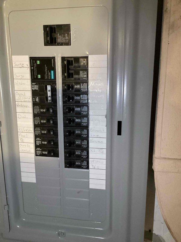Completed electrical inspection correction involving exposed wall cavity and circuit breaker panel. Accessed interior wall opening to inspect and document two gray electrical junction boxes mounted on horizontal blocking, with multiple electrical wires (white, gray, brown, and yellow) properly routed through the cavity and secured with cable clamps. Photographed circuit breaker panel showing properly labeled circuits for all household systems including surge protection, dryer, stove, bedrooms, deck, GFI outlets, and counter receptacles. Verified all electrical connections within junction boxes meet code requirements and documented existing conditions for inspection approval.
