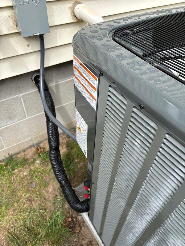 Completed full HVAC system installation including new Goodman furnace and air conditioning unit. Interior furnace installed in basement with proper ductwork connections, humidifier integration, and PVC condensate drainage lines. Exterior Goodman AC unit positioned on concrete pad with electrical disconnect box, proper conduit routing, and refrigerant line connections to complete the system.