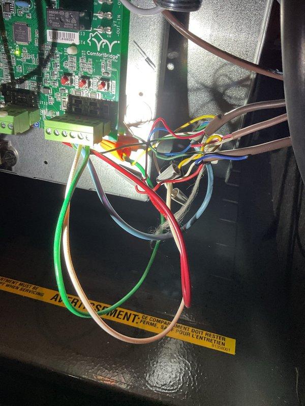 # No Cool Service Call

Responded to a no cooling complaint on a 20-year-old HVAC system. Upon inspection, found the unit blowing warm air. Accessed the control panel and examined the ComfortBridge circuit board, wiring connections, and associated components. Documented the internal control system configuration including the green circuit board with electronic components, terminal blocks, and color-coded wiring harness (red, green, blue, yellow, white, and brown conductors). Verified all wire connections at terminal blocks and wire nuts were secure. Inspected the blue capacitor mounted on the circuit board and checked refrigerant line connections visible in the upper cabinet area. Photographed the control panel assembly and wiring configuration for service records. System evaluated and customer advised of findings.