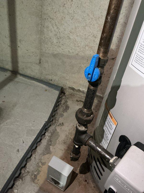 Completed rental inspection of HVAC system and water heater installation. Documented furnace interior components including blower motor assembly, electrical connections with wire nuts, copper refrigerant lines showing age-related oxidation, and ductwork configuration. Inspected water heater plumbing system with blue ball valve shutoff, noting corrosion on metal piping and threaded connections. Verified condensate overflow sensor placement on basement floor and photographed all mechanical equipment for rental property documentation.