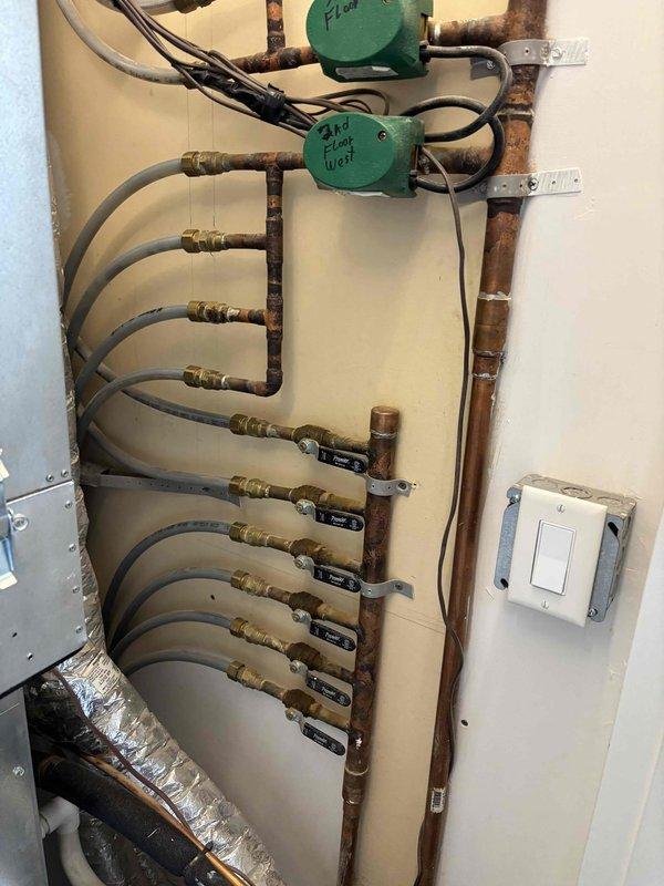 Replaced defective gas valve on hydronic heating system serving multi-floor zone distribution manifold with green circulators labeled for third floor west zone. Completed AC repairs on outdoor condenser unit including cleaning weathered components and verifying proper operation of disconnect and electrical connections.
