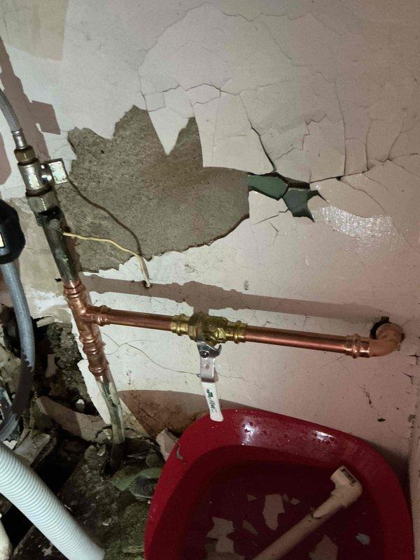 Responded to report of leaking faucet and discovered extensive water damage to interior ceiling and wall with significant material deterioration and exposed plumbing infrastructure. Upon inspection, identified compromised ceiling structure with peeling material and multiple cracks indicating prolonged water intrusion from supply line. Located source of leak at copper pipe connection with brass fittings in affected area. Installed shutoff valve with blue wheel handle on water supply line to isolate the damaged section and prevent further water damage. Collected debris from deteriorated ceiling material for proper disposal. Advised homeowner that extensive drywall and ceiling repair will be required to address structural damage caused by the leak, and recommended consultation with restoration specialist for comprehensive remediation of water-damaged surfaces.