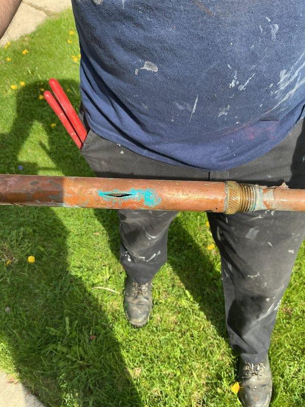 Responded to outdoor spigot leak complaint at residential property built in 1981. Upon inspection, located failed copper supply line beneath exterior siding serving the hose bib. Pipe exhibited severe corrosion and turquoise-blue copper oxidation patina consistent with prolonged moisture exposure and freeze-thaw damage. Isolated the leak source to the corroded section of copper piping with brass fittings. Removed and replaced the deteriorated copper supply line section. Verified no additional plumbing issues present in the system. Leak successfully resolved and outdoor spigot restored to proper operation.