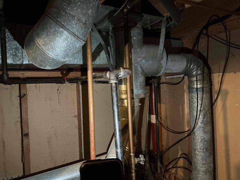 Conducted comprehensive assessment of 30-year-old residential property to provide replacement estimates for HVAC and plumbing systems. Evaluated existing furnace, air conditioner, water heater, and main water pressure regulator for replacement specifications. Inspected basement utility area where galvanized ductwork, copper supply lines, and electrical systems are exposed and accessible. Examined plumbing assembly including multiple copper pipes, ball valves with existing shutoff capabilities, and current water filtration system mounted on utility room wall. Assessed condition of existing infrastructure including oxidized copper piping, brass fittings, and flexible supply lines. Documented mechanical systems layout and spatial constraints for equipment replacement planning. Photographed existing HVAC ductwork configuration, plumbing valve arrangements, and water treatment components to develop accurate replacement specifications. Coordinated dual assessment with comfort advisor to prov