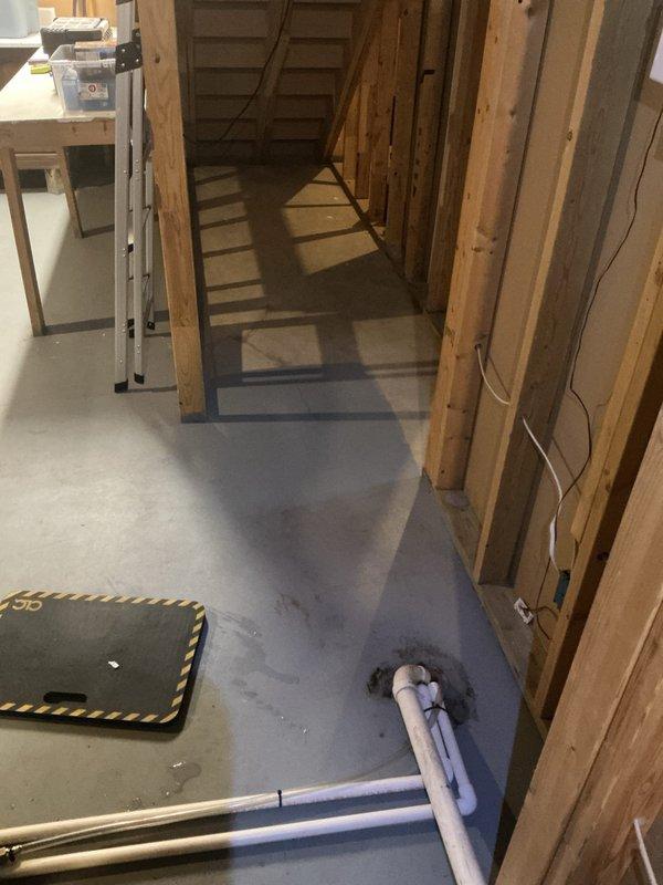 Responded to water leak complaint in basement following recent HVAC installation. Upon arrival, inspected newly installed furnace unit and associated condensate drainage system. Found pooling water on concrete floor near HVAC equipment traced to improper condensate line installation or drainage issues from the furnace unit. Multiple white PVC condensate pipes were routed from the furnace along the floor and up the wall framing. Photographed the installation setup showing the gray furnace unit, condensate piping configuration, and affected floor area. Identified drainage concern related to the new HVAC system installed the previous week requiring correction to prevent continued water accumulation in the basement space.