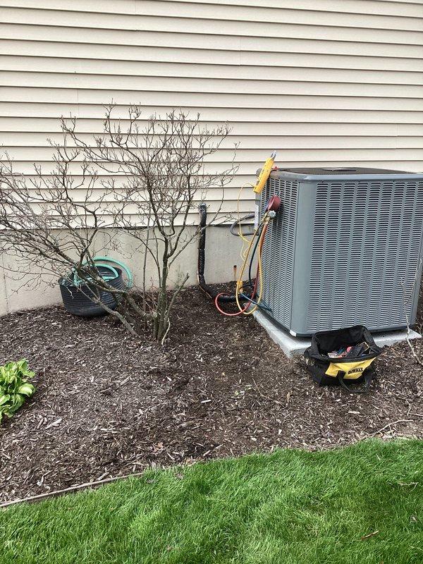 Completed full air conditioning system replacement at residential property. Removed existing outdoor condenser unit and installed new gray metal AC condenser unit on exterior wall with beige vinyl siding, positioned on mulched landscaping area. Ran new refrigerant lines (copper and insulated) from condenser to building with proper mounting brackets and hangers secured to exterior wall. Connected all electrical and refrigerant connections, performed vacuum and pressure testing of system, and charged unit to manufacturer specifications. Verified all utility connections including proximity to gas meter assembly were properly maintained. System tested and operational upon completion.