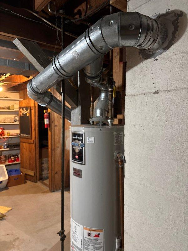 Responded to water heater leaking from base. Upon inspection, confirmed active leak originating from the bottom of the unit, indicating internal tank failure. Explained to customer that leaks from the base typically result from sediment buildup and corrosion over time, which compromises tank integrity and cannot be repaired. Recommended full water heater replacement as the only viable solution. Customer approved replacement. Shut off water supply and gas line to existing unit, drained tank completely, and disconnected all water lines, gas connections, and venting system. Removed failed water heater from basement mechanical room. Installed new white cylindrical water heater in same location against wall. Connected cold water inlet and hot water outlet lines to top of unit using appropriate fittings. Reconnected gas supply line with black pipe and verified all connections for proper seal. Installed metallic ductwork and flexible corrugated venting to exhaust combustion gases safely throu